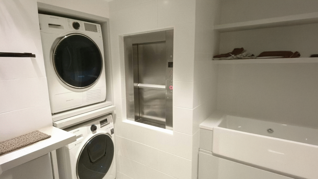 A wall-mounted laundry dumbwaiter featuring a square metal door that opens to a small lift compartment used for transporting clothes between floors. dumbwaiters